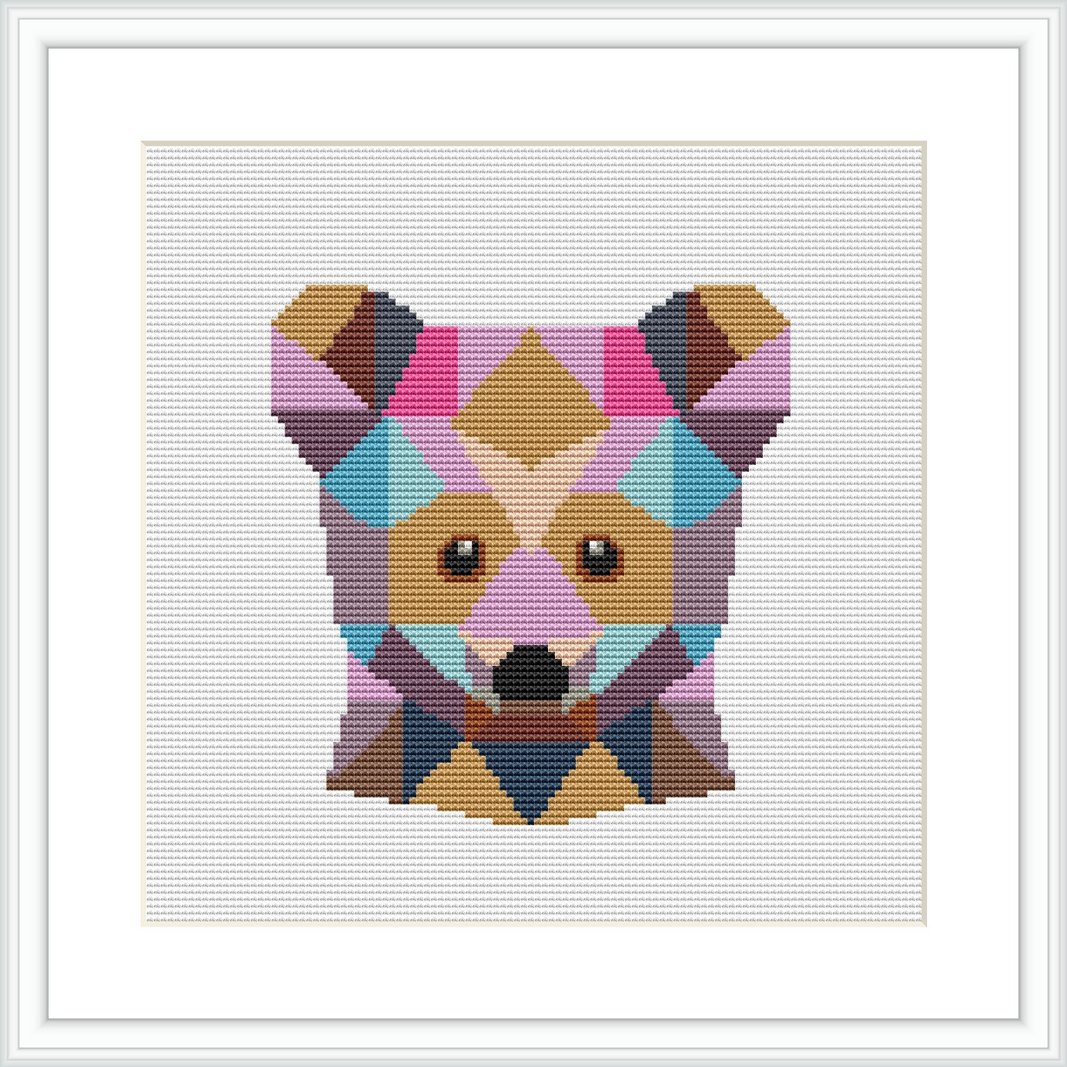 The image shows a framed cross stitch pattern of a bear's face, composed of various geometric shapes in a range of pastel colors. The pattern is centered and showcased within a square frame against a white background.