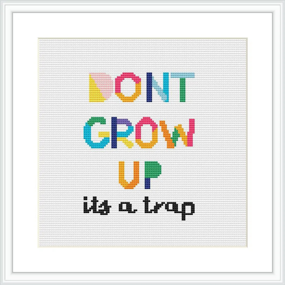 The image displays a white square cross stitch fabric with a colorful text pattern that reads 'DON'T GROW UP it's a trap' in bold, stylized letters. The letters are in multiple colors and on a white background, framed with a simple white border.