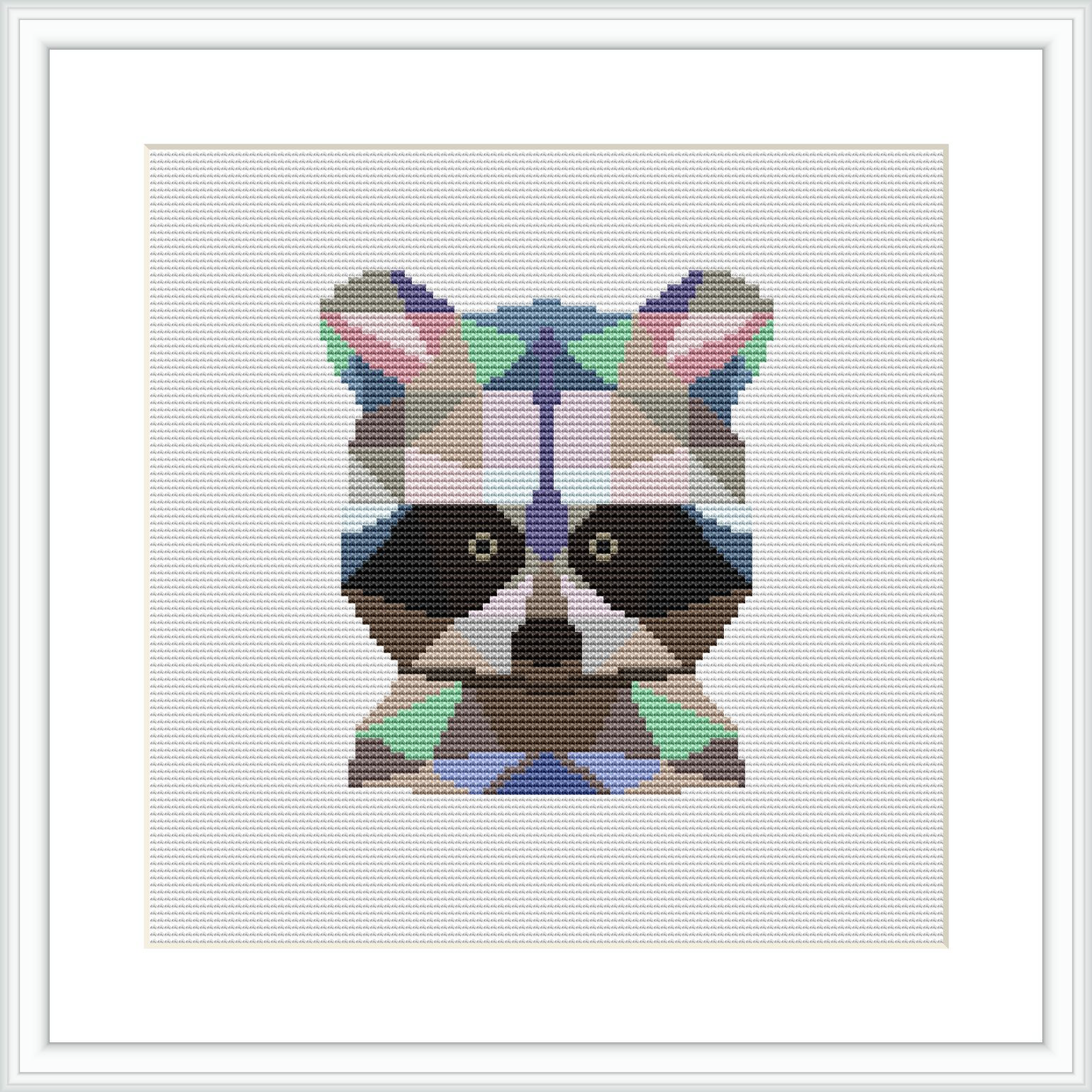 The image depicts a framed cross stitch piece featuring a stylized raccoon face comprised of geometric shapes. The raccoon is centered on a white fabric background and is rendered in a variety of colors including earth tones and vibrant accents.