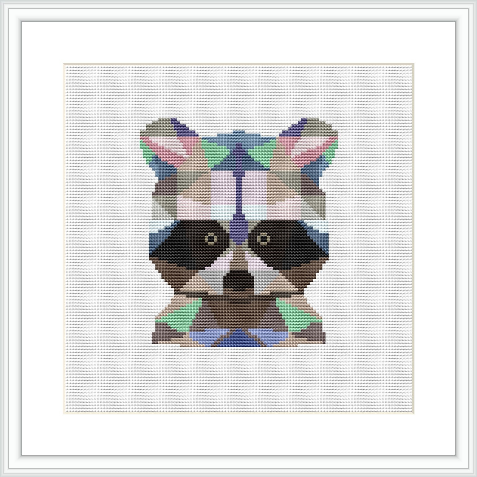 The image depicts a framed cross stitch piece featuring a stylized raccoon face comprised of geometric shapes. The raccoon is centered on a white fabric background and is rendered in a variety of colors including earth tones and vibrant accents.