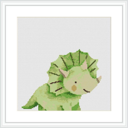 The image displays a cross stitch pattern of a green dinosaur with a pale yellow underbelly. Its eyes are closed, suggesting a serene or sleepy expression. The dinosaur is set against a white background within a framed canvas.