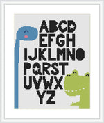 A cross stitch pattern displaying a blue dinosaur on the left and a green dinosaur on the right with the alphabet letters 'A' to 'Z' in black spread among them. The pattern is framed with a simple border and showcased against a white background.