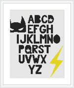 A cross stitch pattern featuring a superhero-like bat figure at the top, with a full alphabet below it. On the bottom right, there's a lightning bolt symbol. All design elements are in stylized fonts and shapes, using a limited color palette.