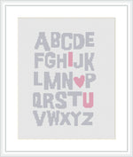 A cross stitch pattern featuring the uppercase English alphabet where specific letters are highlighted to read 'I LOVE YOU' with a heart symbol substituting for the letter 'O'. The letters are arranged in a neat grid with alternating colors in pink and gray against a white background.