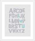 The image depicts a framed cross stitch pattern showing a simple alphabet design where the letters 'I' and 'U' are distinguished in a mint green color, and a heart shape replaces the letter 'O', also in mint green. The background is white and the letters are in a soft grey.