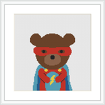 The image shows a cross stitch pattern of a bear character donning a superhero costume with a red mask and cape, a blue suit, and a yellow emblem and belt, centered on a white canvas surrounded by a white frame.