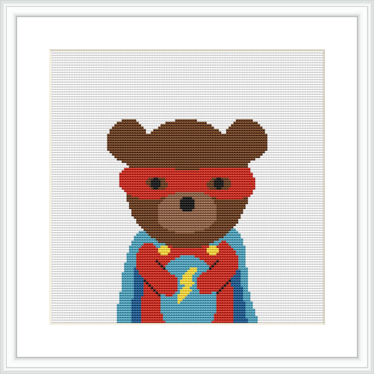 The image shows a cross stitch pattern of a bear character donning a superhero costume with a red mask and cape, a blue suit, and a yellow emblem and belt, centered on a white canvas surrounded by a white frame.