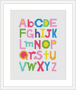 The image displays a cross stitch pattern of the English alphabet where each letter is stitched in a different and vibrant color. The letters are styled in block fonts with varying designs and are arranged in alphabetical order across the canvas. The pattern is framed with a simple white border.