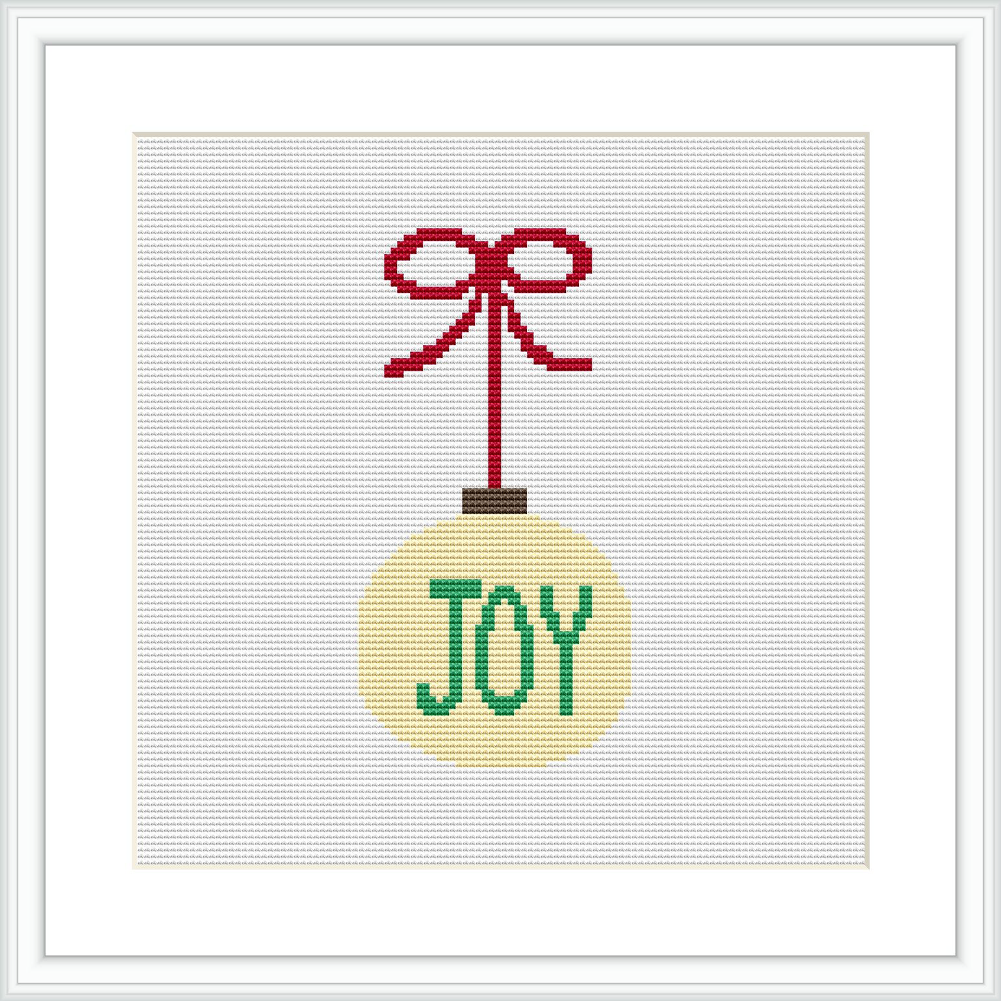 The image shows a digitally rendered cross stitch pattern of a Christmas ornament. The ornament is round and gold with a red ribbon tied in a bow at the top, and it has the word 'JOY' in green letters across the center. The design is displayed within a square white frame on a grey background.