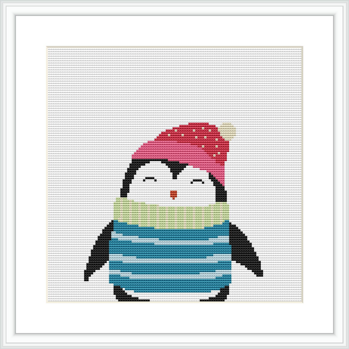 This is an image of a cross stitch pattern featuring a cartoon-style penguin. The penguin is wearing a red hat with a yellow pom-pom and a green and blue striped scarf. The penguin is depicted in a standing position against a plain white background, framed in a simple white frame.