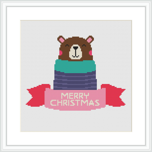The image shows a cross stitch design featuring a brown bear wearing a pink Santa hat and partially wrapped in a gift box with layers of green, blue, and purple. The words 'MERRY CHRISTMAS' are stitched in red on a banner below the bear.
