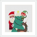 This cross stitch pattern displays Santa Claus in his traditional red and white suit at the center, with a green Christmas tree behind him. An elf is perched atop the tree placing a yellow star, with strands of lights wrapped around them. At the base, there's a brown reindeer tangled in lights.