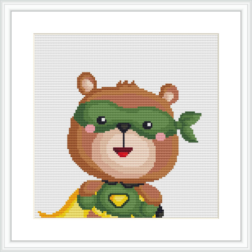 The image displays a cute, cartoon-style bear wearing a green mask and a hero’s cape. The bear also has a green emblem on its chest, all crafted using cross stitch technique on a white background.