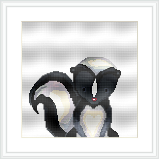 The image showcases a framed cross stitch pattern featuring a stylized skunk with a heart-shaped white pattern on its forehead and chest, positioned against a plain background.