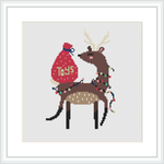 The image depicts a cross stitch pattern of a brown reindeer with antlers, wrapped in green Christmas lights, carrying a red bag saying 'TOYS'. It's framed with a simple black border on a white background.