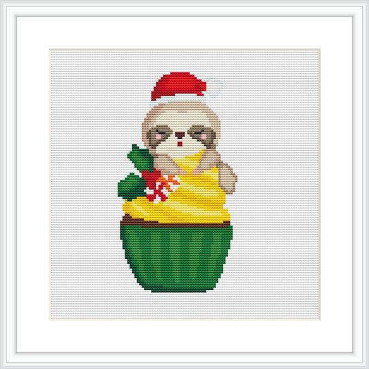 The image shows a cross stitch pattern of a sloth wearing a Santa hat, sitting inside a green cupcake liner. The sloth holds a sprig of holly with red berries. The background is plain white.