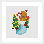 This cross stitch pattern displays a smiling sloth with red bows on its ears, wrapped in green Christmas socks decorated with patterns including Christmas trees. The sloth appears cozy and content against the white background of the canvas.