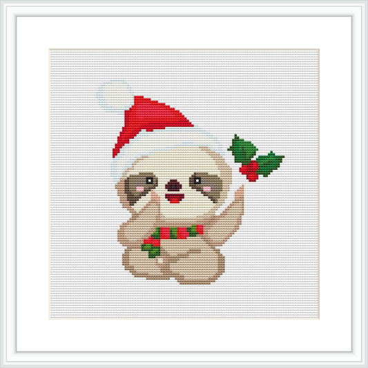 The image displays a cross stitch pattern of a cute sloth wearing a red Santa hat. To the right of the sloth, there are green holly leaves with red berries. The pattern is centered on a white canvas grid, framed in white, presenting a clear and focused depiction.