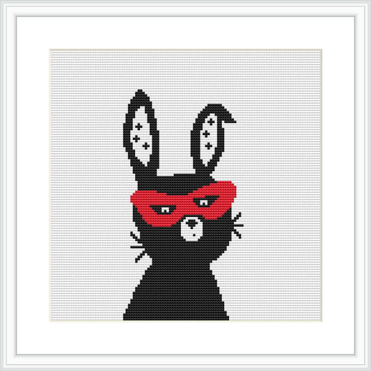 The image features a stylized bunny with a superhero mask, predominantly in black and white with a striking red mask, framed within a classic cross stitch hoop against a white backdrop.