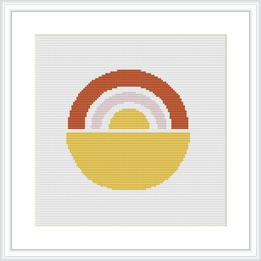 The image presents a framed cross stitch pattern depicting geometric shapes resembling a semi-circle or rainbow. It is stitched on a square fabric and is placed in a simplistic white frame.