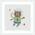 The image displays a cross stitch pattern of a cartoony bear dressed as an astronaut surrounded by stars. The bear is in space, with a half-moon and two individual stars placed near it. The background is plain white.