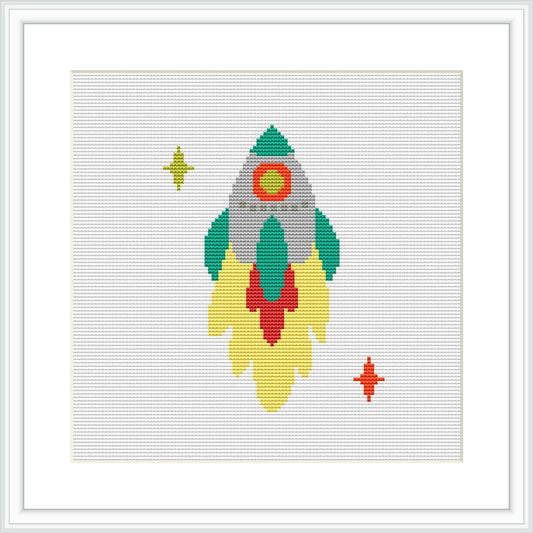 The image showcases a cross stitch pattern of a stylized space rocket with flames at the bottom, accompanied by two stars, one larger on the left and a smaller one on the right.