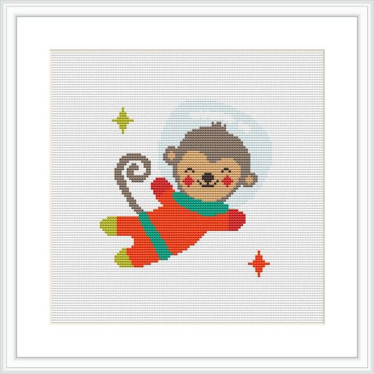 The image showcases a cross stitch pattern depicting a cartoon-like monkey in a red and green spacesuit, surrounded by a light blue halo representing space. There are small yellow and red stars scattered around the monkey.