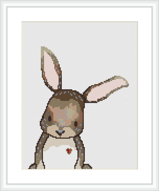 The image depicts a cross stitch pattern of a bunny figure with a watercolor effect. The bunny is centered on the fabric, with its ears upright and a tiny red heart detail on its chest.