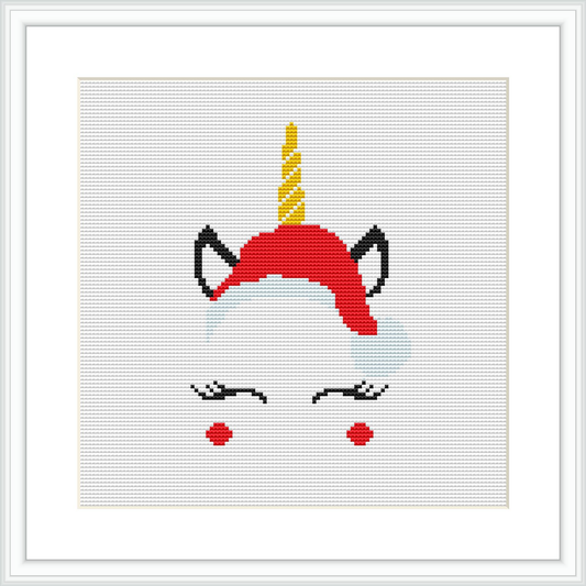 The image shows a simplistic and stylized representation of a unicorn's head wearing a red Christmas hat, with a gold-colored horn, closed eyes with lashes, and rosy cheeks. The design is framed within a square frame with a white border against a neutral background.