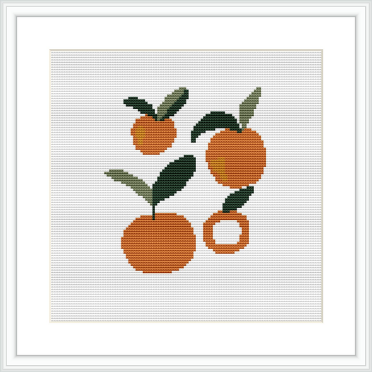 The image shows a cross stitch pattern featuring three Valencia oranges with green leaves. Two oranges are whole and one is cut, with all pieces placed against a white background within a square frame.