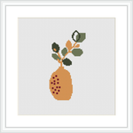 The image shows a cross stitch pattern featuring a stylized branch of a citrus tree with leaves and fruit, contained in a simple brown pot. The pattern is rendered in warm colors against a white background.