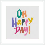 The image shows a cross stitch pattern with the phrase 'Oh Happy Day!' stitched in colorful block letters on a white canvas framed in a simple white frame.