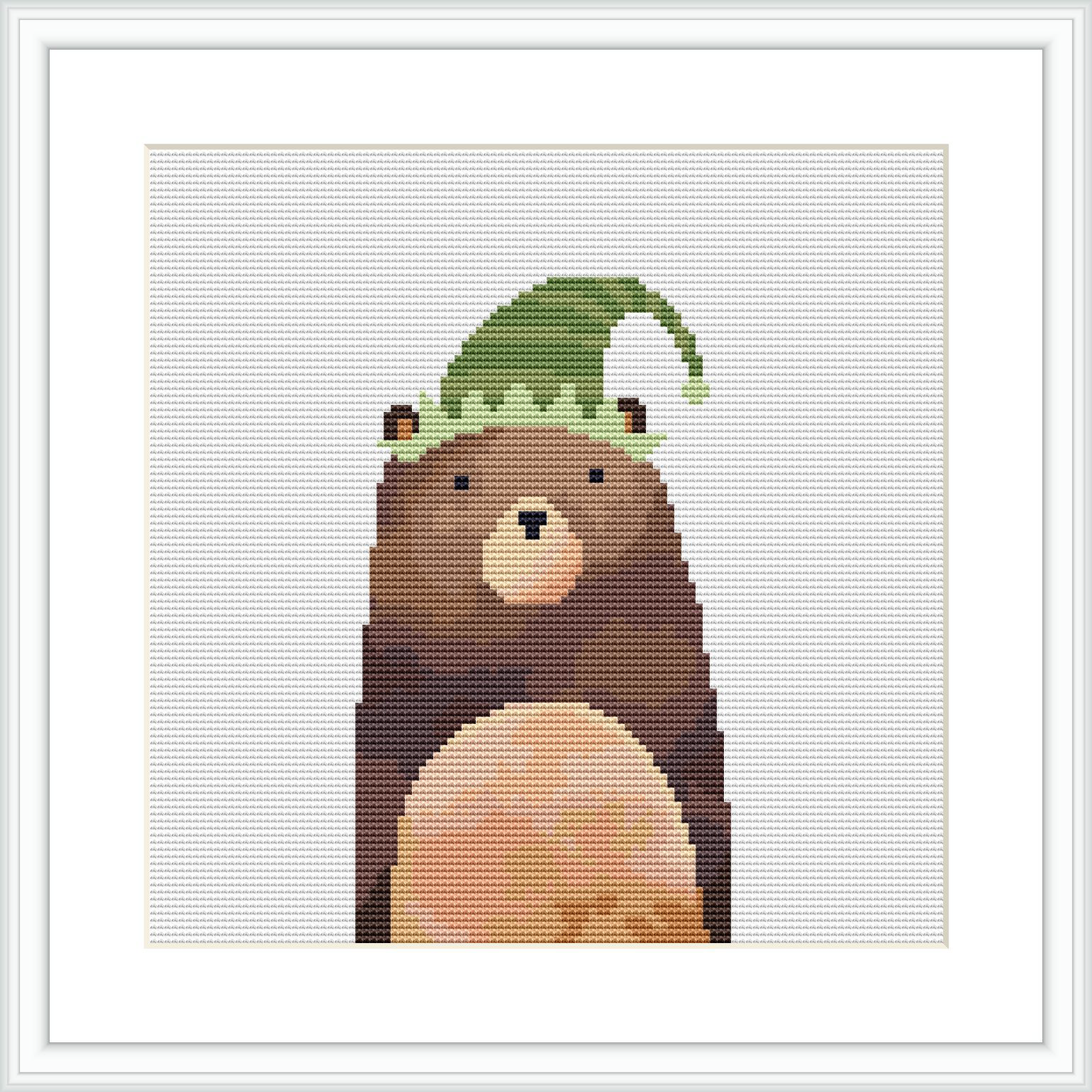 The image shows a cross stitch pattern of a bear with a humorous elf hat on its head. The bear is centered on the canvas, with stitched eyes, nose, and a large round belly visible. The elf hat is green with a curved tip as if drooping down.