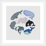 The image shows a framed cross stitch piece with various whales arranged in a pattern. The designs are pixelated due to the cross stitch technique and are depicted in shades of blue, grey, and white, with touches of pink and black.