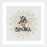 The image displays a cross stitch pattern featuring the phrase 'Life is Beautiful' centered on a white canvas. The text is surrounded by radial lines that create a sunburst effect, primarily in gold and black tones.