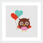 The image displays a framed cross stitch pattern showing a brown owl with white accents and glasses. The owl is holding three heart-shaped balloons—two above its head and one held by its wing. The balloons are colored red and teal. This representation is set against a plain white background and is contained within a square frame.