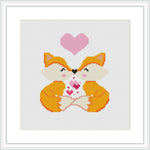 The image shows a cross stitch pattern featuring two mirrored foxes with a shared gaze, forming a heart with their outlines. Above them is a larger heart symbol. The design is contained within a white square frame.