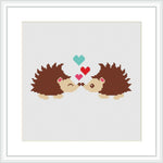 The image shows a framed cross stitch pattern of two brown and tan porcupines facing each other with their noses touching. Above them, three hearts in shades of blue, red, and pink float upwards. The background is plain white.