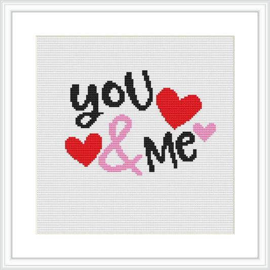 The image displays a cross stitch pattern featuring the phrase 'you & me' in stylized typography with two red and one pink heart shaped figures. The background is white, and the phrase consists of black, red, pink, and gray colors. The design is framed within a simple square frame, suggesting a modern and clean aesthetic.