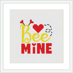 This cross stitch pattern features the words 'Bee Mine' with the 'Bee' part written in yellow and the 'Mine' in red. Above the 'Bee' is a red heart and two bees, one at each end of the phrase. The background is white, and the pattern is contained within a square frame.