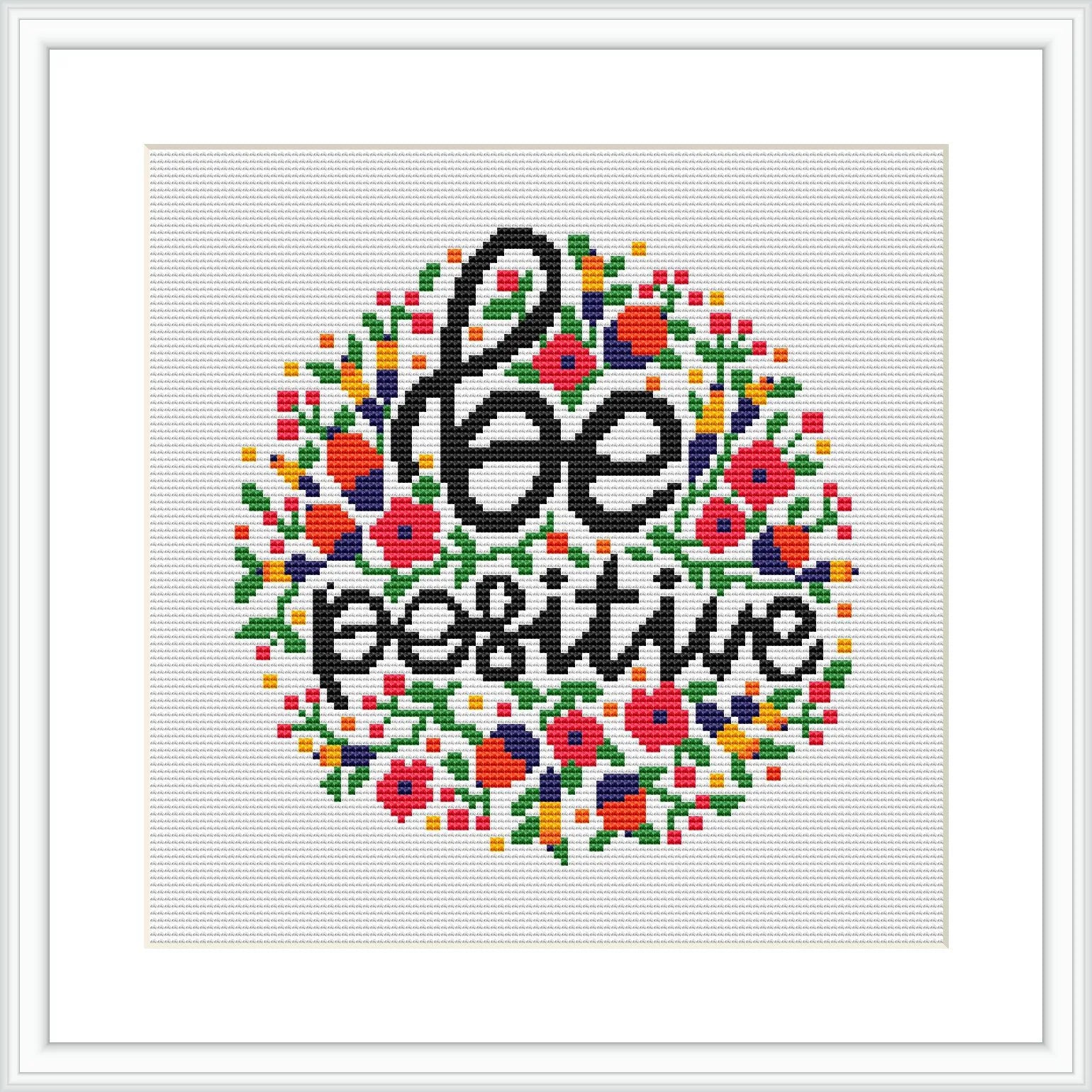 The image displays a cross stitch pattern featuring the phrase 'Be Positive' at the center, surrounded by a circular floral border. Various colors are used to create the flowers and leaves, which are symmetrically arranged around the central text. The pattern is presented on a white background within a framed piece.