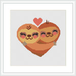 A framed cross stitch pattern depicting two sloths hugging inside a large heart shape with a small heart above them, set against a white background.