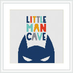 The image features a cross stitch pattern with the phrase 'LITTLE MAN CAVE' in colorful block letters at the top and the silhouette of a stylized superhero mask in blue at the bottom, all centered against a white background within a frame.