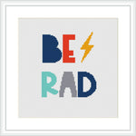 The image displays a framed cross stitch pattern featuring the phrase 'BE RAD' with each letter in a different bold color. The letter 'E' is replaced with a lightning bolt in a contrasting color.