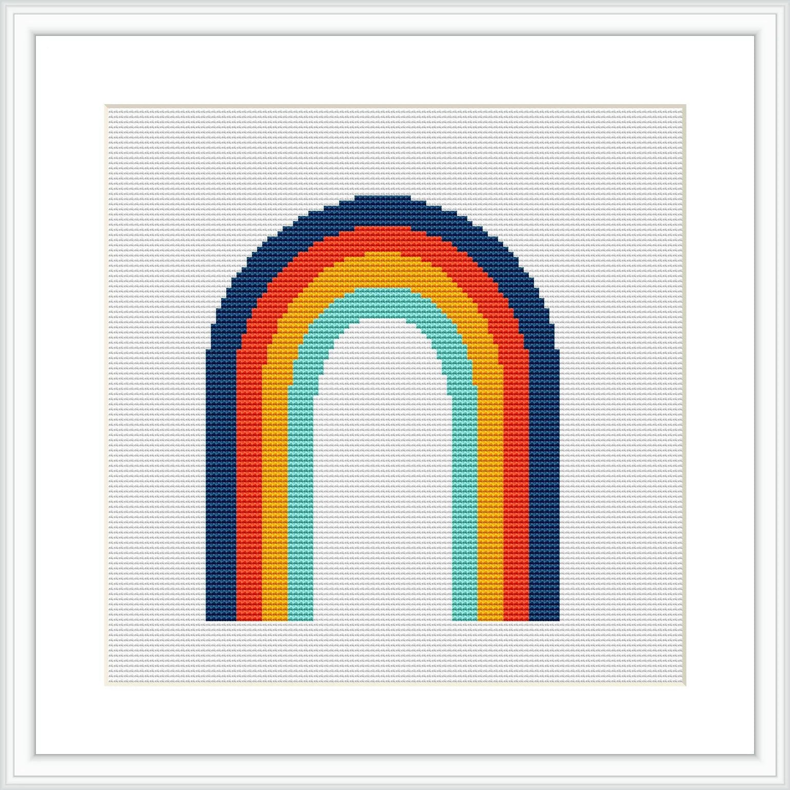 The image shows a framed cross stitch pattern of a rainbow with six colored bands: red, orange, yellow, green, blue, and indigo, on a white background and within a square frame.