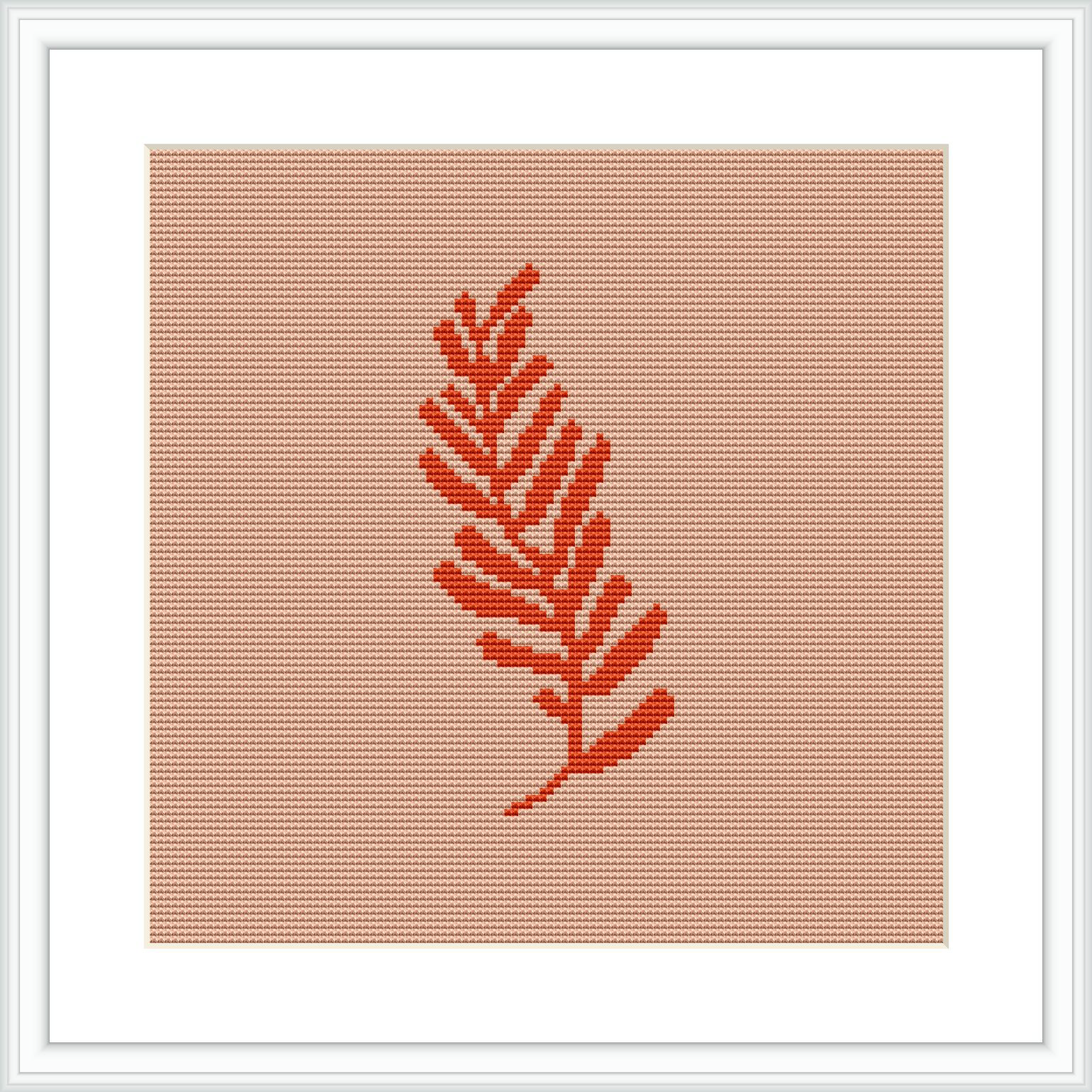 The image presents a single, coral-colored fern leaf centered on an even-weave fabric. The design is framed within a white square border, suggesting it is likely a cross stitch piece ready for display.