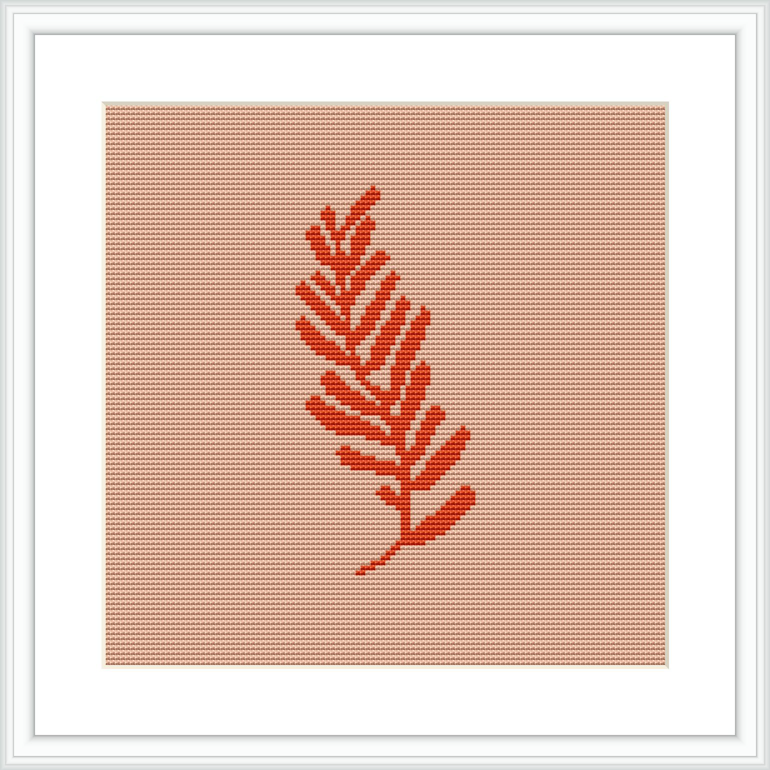 The image presents a single, coral-colored fern leaf centered on an even-weave fabric. The design is framed within a white square border, suggesting it is likely a cross stitch piece ready for display.