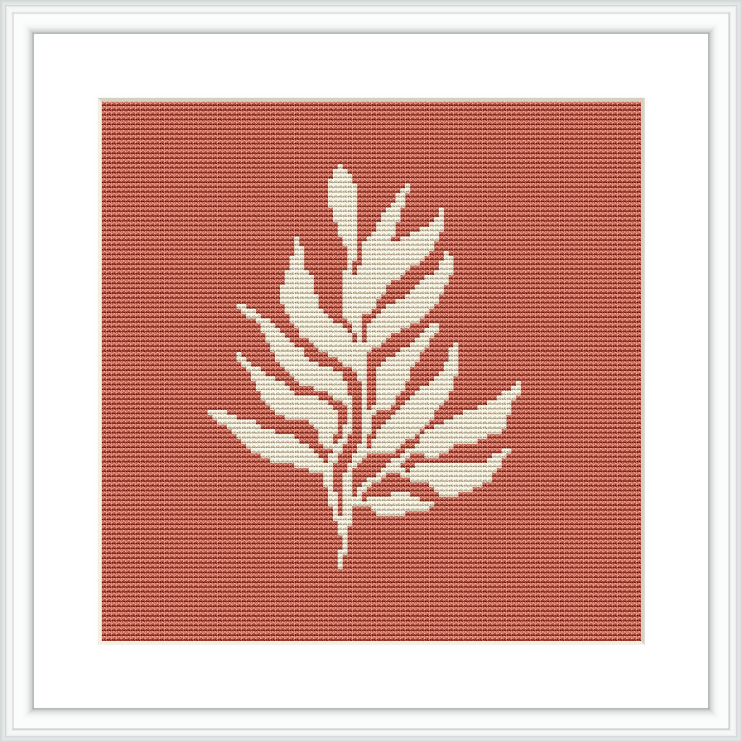 The image displays a framed cross stitch pattern with a minimalist plant motif in white against a crimson background. The pattern is centered within a square frame, suggesting a modern aesthetic.