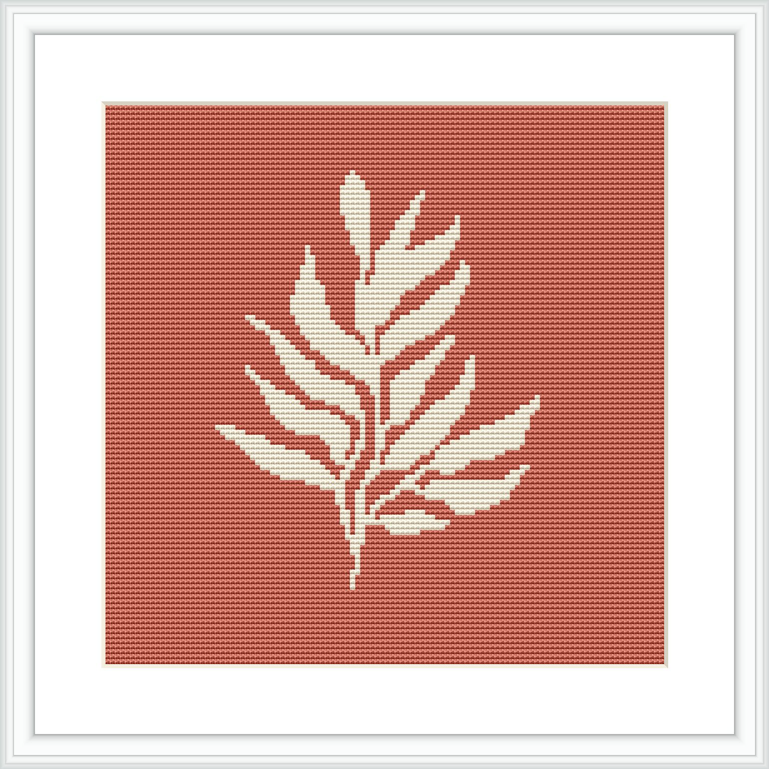 The image displays a framed cross stitch pattern with a minimalist plant motif in white against a crimson background. The pattern is centered within a square frame, suggesting a modern aesthetic.