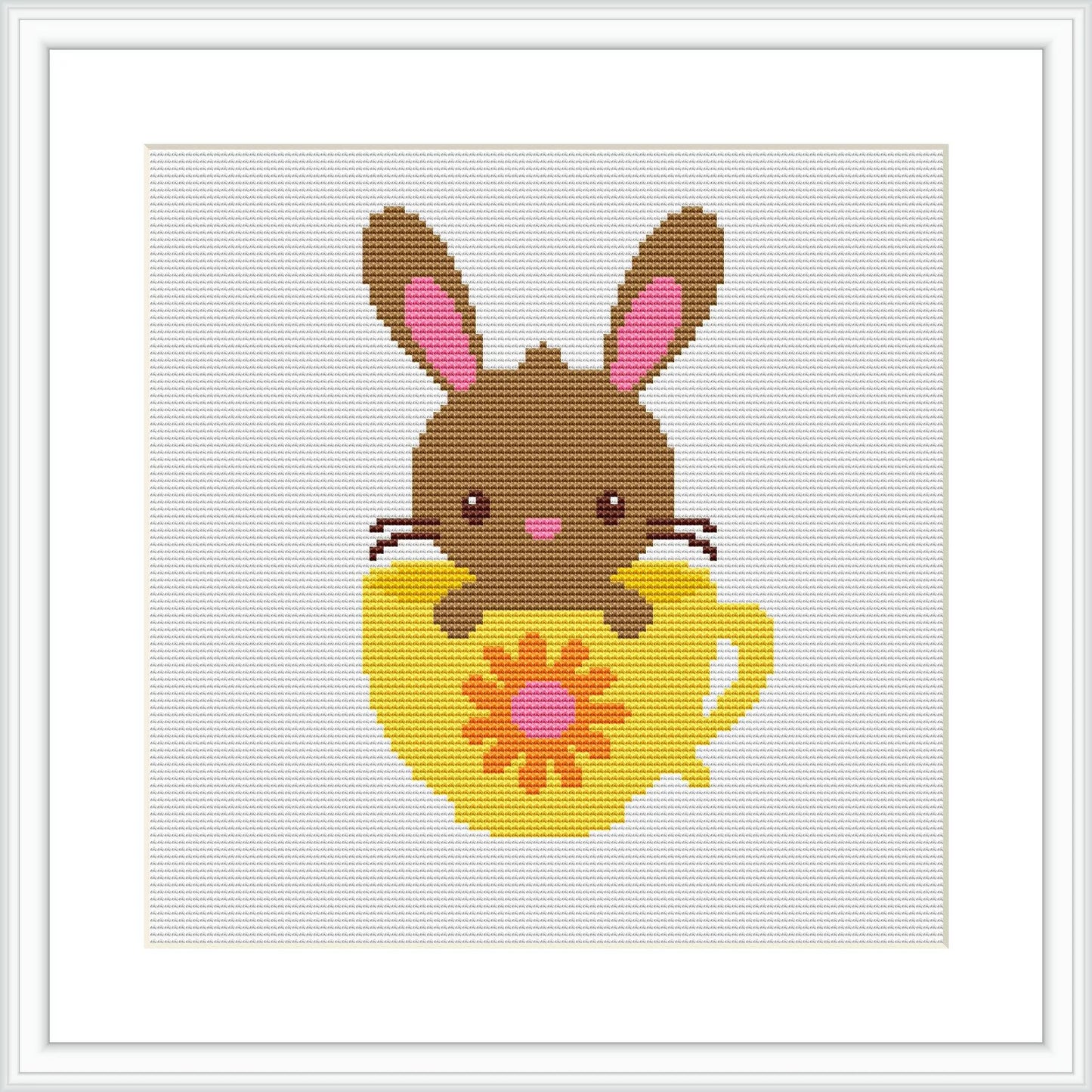 The image shows a cross-stitch pattern depicting a brown bunny with pink inner ears and blushing cheeks sitting inside a yellow egg-shaped cup with a red floral design on it. The background is white, and the pattern is framed with a simple square frame.